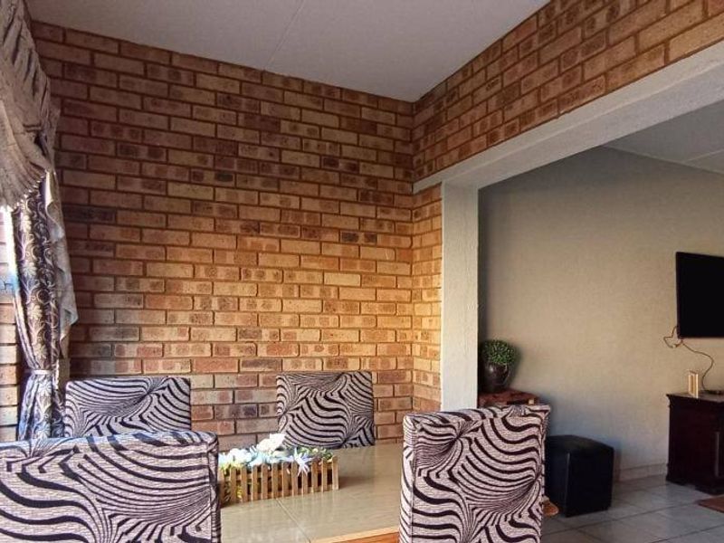 Open-plan living and dining area featuring an exposed brick feature wall, tiled flooring, and large sliding glass doors providing natural light.