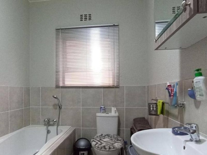 A functional bathroom featuring a bathtub, toilet, and washbasin with a wall-mounted vanity cabinet and neutral wall tiling.