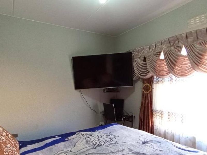 A bedroom featuring a wall-mounted television and window treatments.