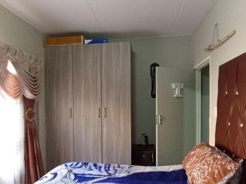 A bedroom featuring a built-in wardrobe with wood-grain finish and a window with decorative pelmet.