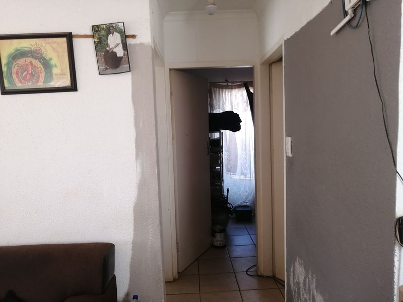 A residential hallway featuring tiled flooring and internal access doors, currently showing signs of unfinished wall maintenance and wear.