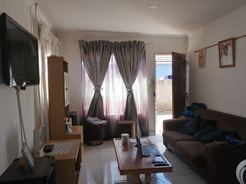 A compact living room featuring tiled flooring and direct access to an outdoor area, providing a functional space with potential for cosmetic updates.