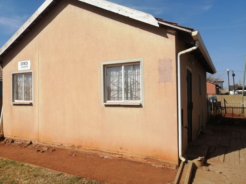 A view of the front exterior facade of a single-story house featuring plastered walls, security bars on windows, and functional guttering.
