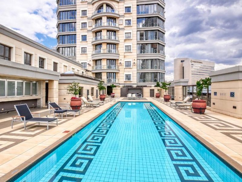 A well-maintained outdoor swimming pool area featuring a tiled deck, stone building facade, and modern architectural design in an apartment complex setting.