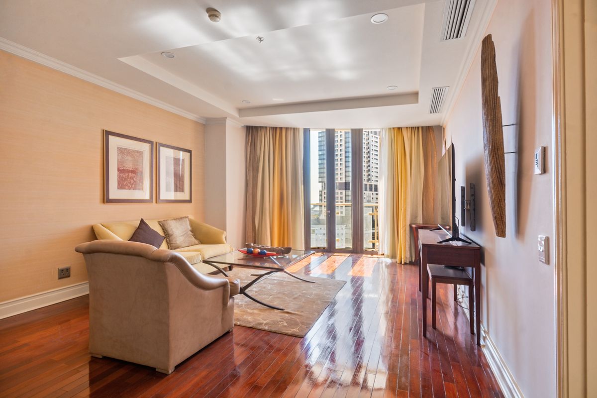 A well-maintained living room featuring polished hardwood flooring, recessed lighting, ducted air conditioning, and direct access to a balcony with city views.