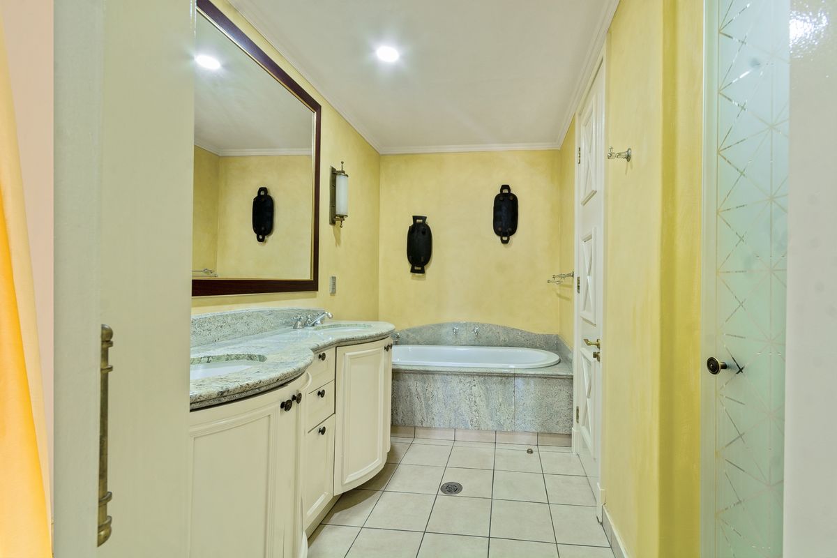 A well-maintained bathroom featuring a double vanity with granite countertops, a built-in bathtub, and a separate shower enclosure with patterned glass.