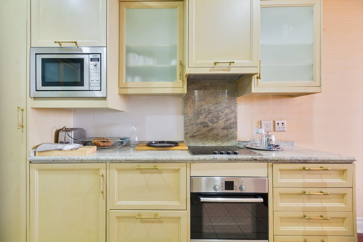 A well-maintained kitchen featuring cream-toned cabinetry, granite countertops, and integrated appliances including an oven, hob, and microwave.