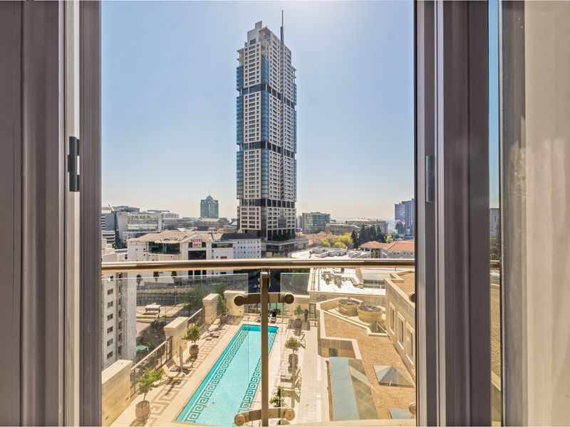 Elevated urban view overlooking a swimming pool terrace and surrounding city skyline from an apartment window.