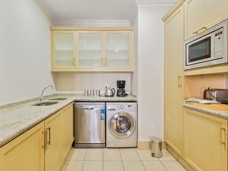 A functional scullery featuring built-in cabinetry, granite countertops, a double basin sink, and integrated microwave, providing ample storage and utility space.