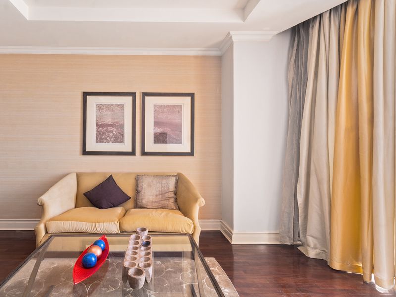 A well-maintained living room featuring rich hardwood flooring, elegant crown molding, recessed ceiling details, and neutral textured wallpaper.