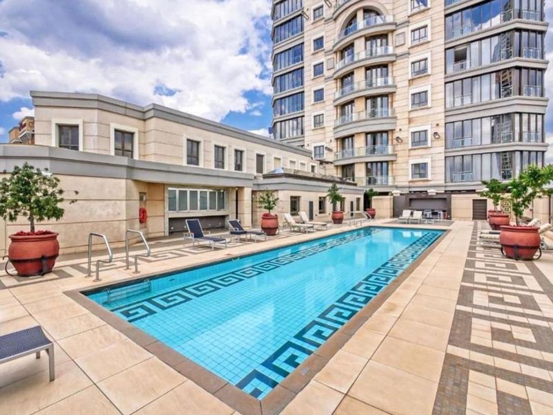 A well-maintained outdoor swimming pool area featuring a tiled deck, set against a modern apartment building with balconies.