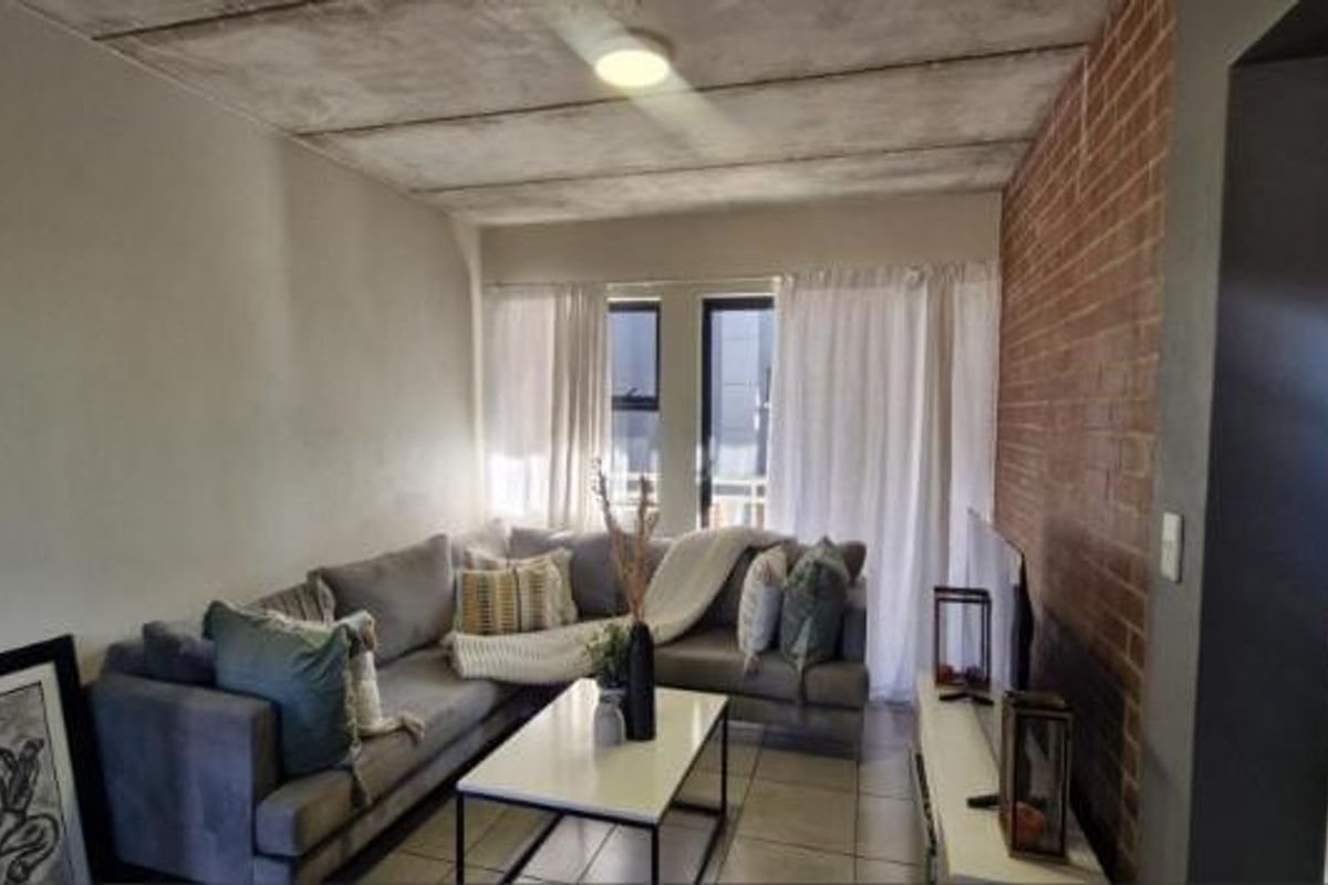 Living room featuring an exposed brick feature wall and industrial-style exposed concrete ceiling with tiled flooring.