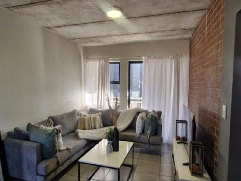 Living room featuring an exposed brick feature wall and industrial-style exposed concrete ceiling with tiled flooring.