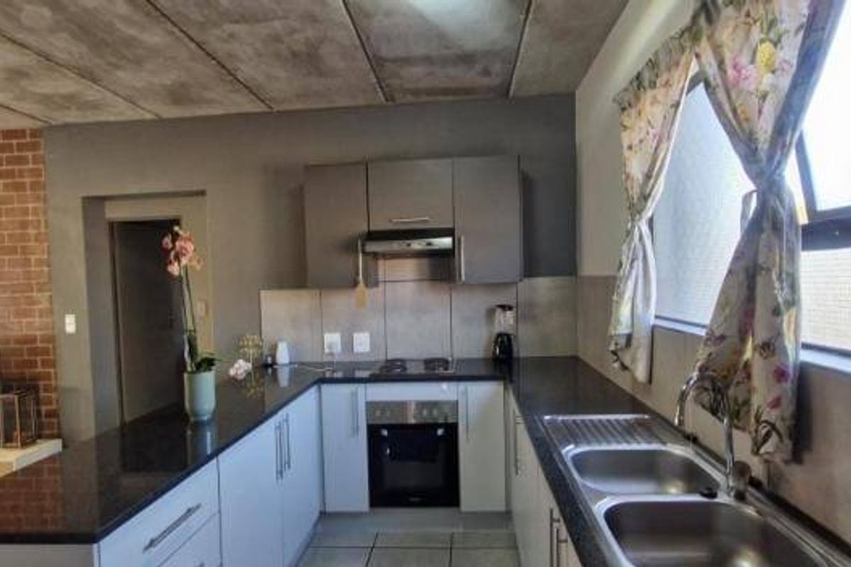 Modern open-plan kitchen featuring granite countertops, built-in oven, hob, and extractor fan, complemented by an exposed brick wall and concrete ceiling.