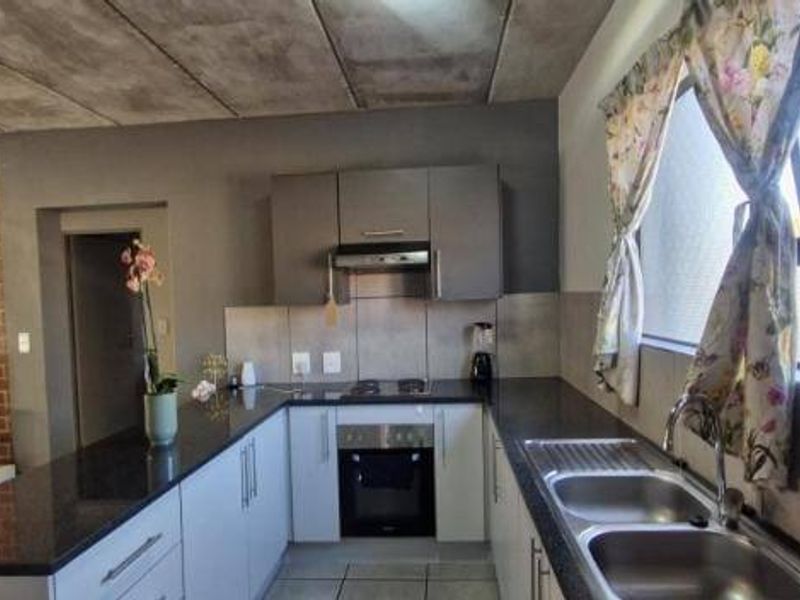 Modern open-plan kitchen featuring granite countertops, built-in oven, hob, and extractor fan, complemented by an exposed brick wall and concrete ceiling.