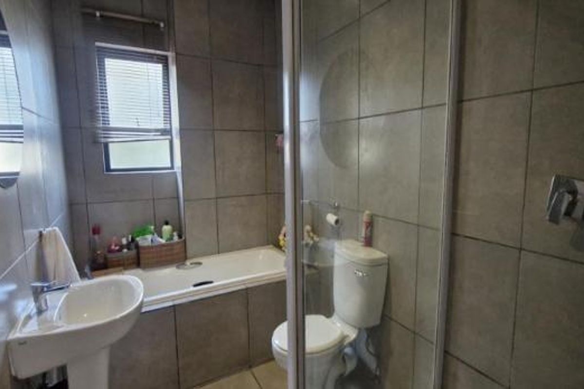 A functional bathroom featuring a pedestal basin, built-in bathtub, separate shower enclosure, and toilet with neutral wall and floor tiling.
