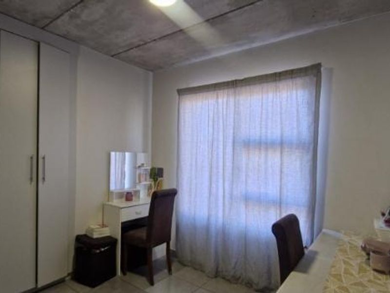 A bedroom featuring built-in cupboards, tiled flooring, and an exposed concrete ceiling, providing a modern industrial aesthetic.