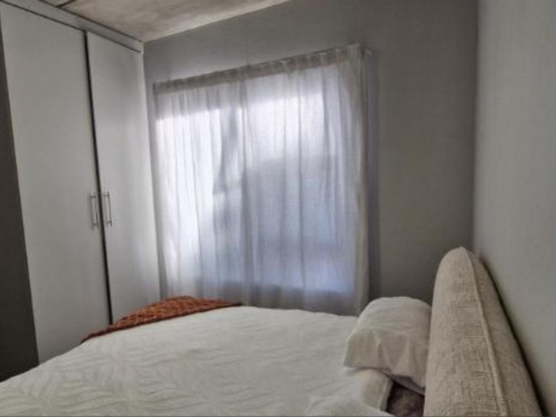 A functional bedroom featuring a built-in wardrobe and natural light through a window with sheer curtains.
