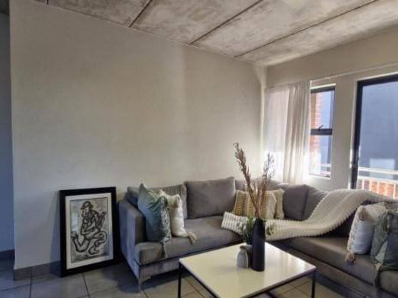 A living room featuring an exposed concrete ceiling, tiled flooring, and a sliding glass door providing natural light.