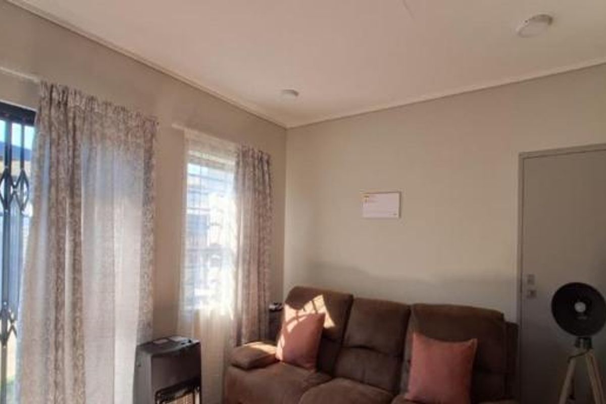 A bright living room featuring a sliding glass door with security gate, providing access to the outdoor area and natural light.