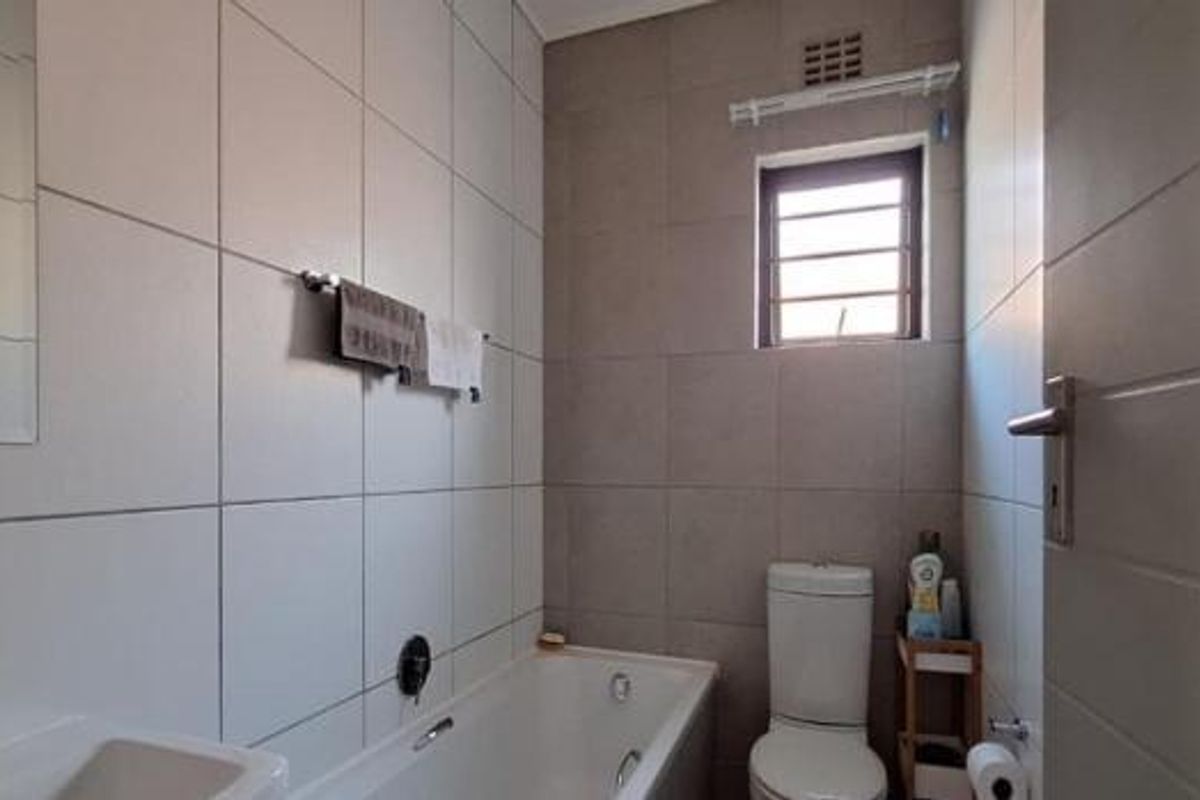 A clean, functional bathroom featuring a bathtub, toilet, basin, and neutral wall tiling with a window for natural light.