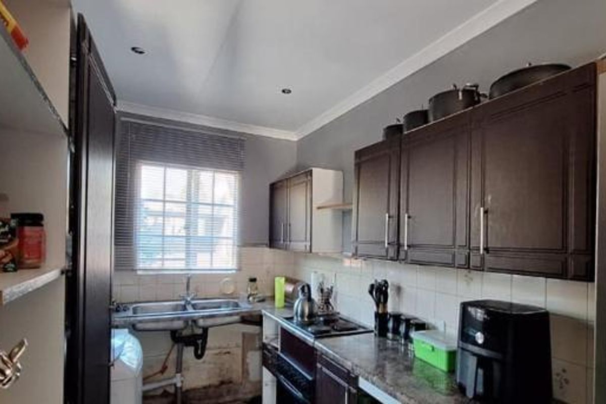 Compact kitchen featuring dark cabinetry, laminate countertops, tiled splashback, and a double basin sink with exposed plumbing requiring cosmetic attention.