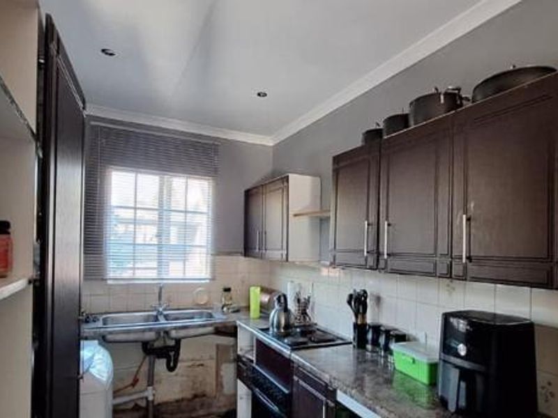 Compact kitchen featuring dark cabinetry, laminate countertops, tiled splashback, and a double basin sink with exposed plumbing requiring cosmetic attention.