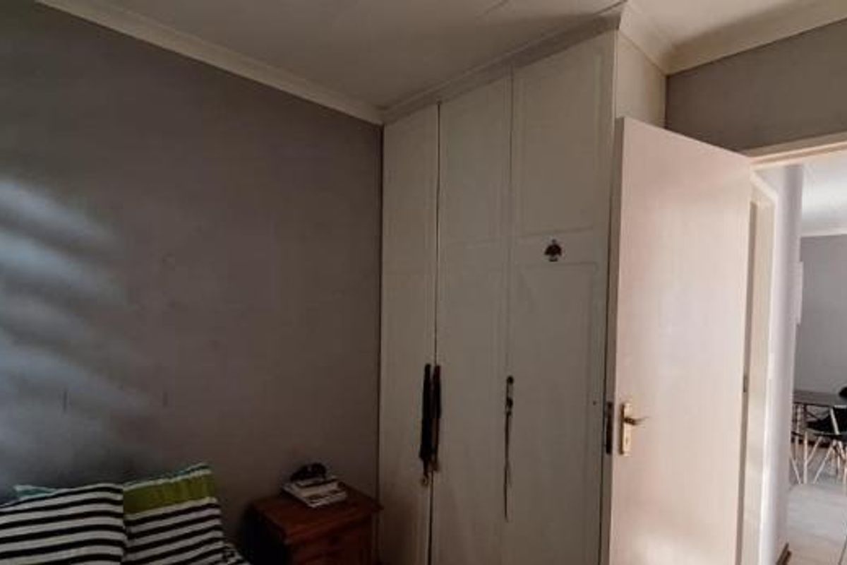 A bedroom featuring built-in cupboards and coving, with a view through the doorway into an adjacent living area.