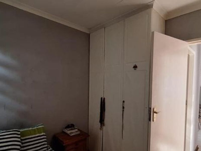 A bedroom featuring built-in cupboards and coving, with a view through the doorway into an adjacent living area.