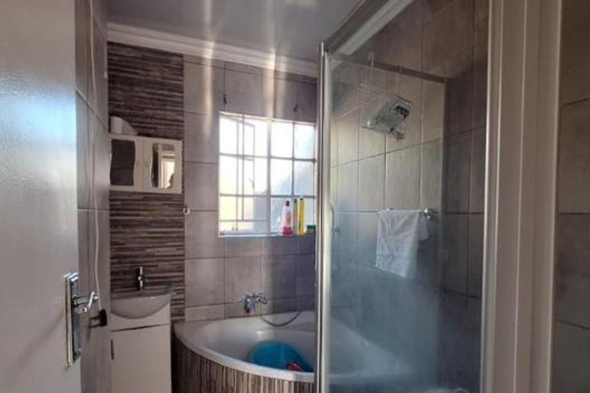 A functional bathroom featuring a corner bathtub, a separate glass-enclosed shower, and a wall-mounted basin with tiled finishes.