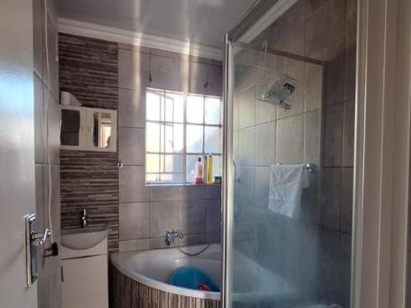 A functional bathroom featuring a corner bathtub, a separate glass-enclosed shower, and a wall-mounted basin with tiled finishes.