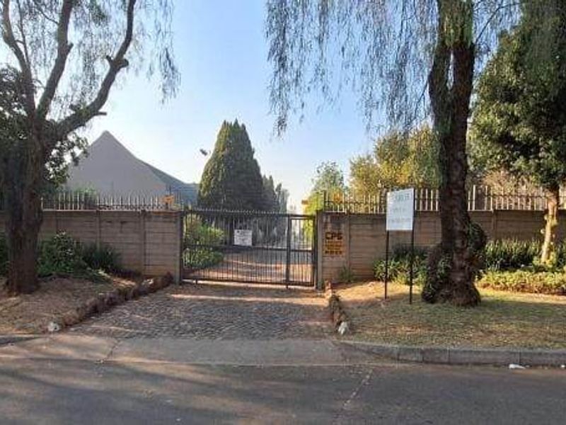 Street view of the apartment complex entrance featuring a secure gated access point, perimeter walling, and communal post boxes.