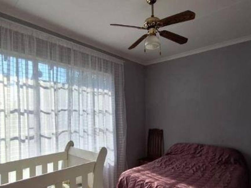 A bedroom featuring grey walls, a ceiling fan, and large windows with sheer curtains, providing a neutral base for potential interior updates.