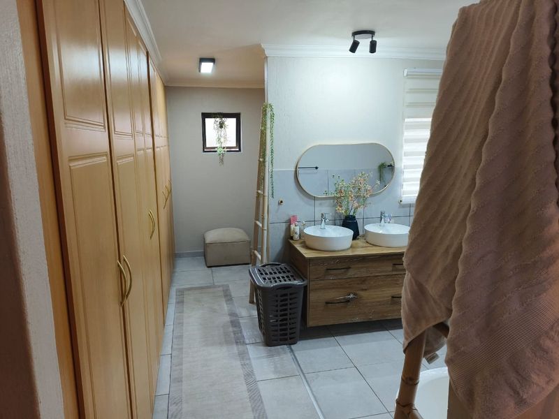 A well-maintained bathroom featuring a double vanity with vessel sinks, ample built-in cupboard storage, and modern tiled flooring.