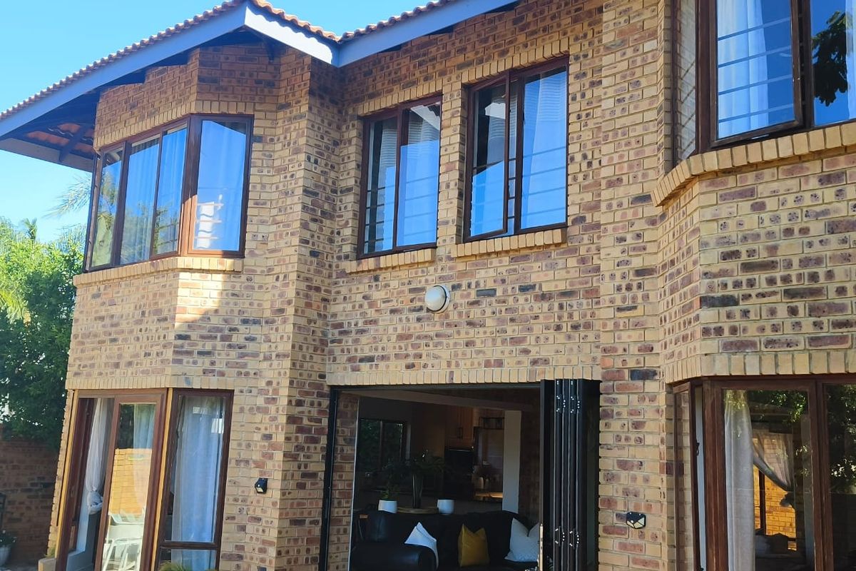 Rear elevation of a double-story face brick house featuring large bay windows and modern folding stacker doors opening to the interior living space.