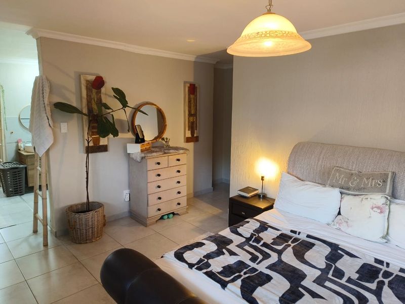 A bedroom featuring tiled flooring and a central ceiling light fixture, with an adjoining space visible through the doorway.