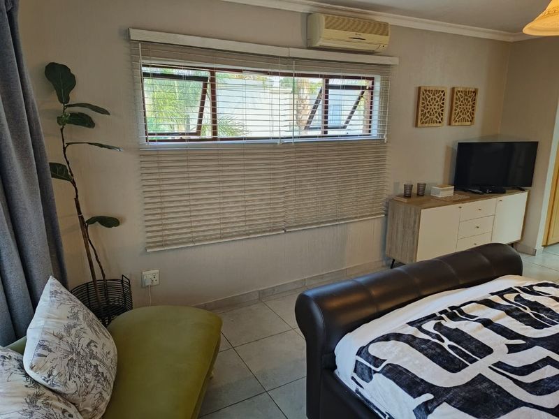 A well-maintained bedroom featuring tiled flooring, a wall-mounted split-system air conditioner, and horizontal window blinds.