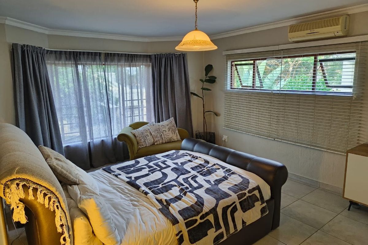 A well-lit bedroom featuring tiled flooring, a split-system air conditioner, and large windows with fitted blinds, offering a comfortable and functional living space.