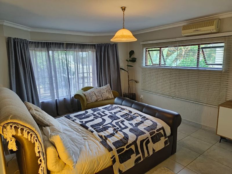 A well-lit bedroom featuring tiled flooring, a split-system air conditioner, and large windows with fitted blinds, offering a comfortable and functional living space.