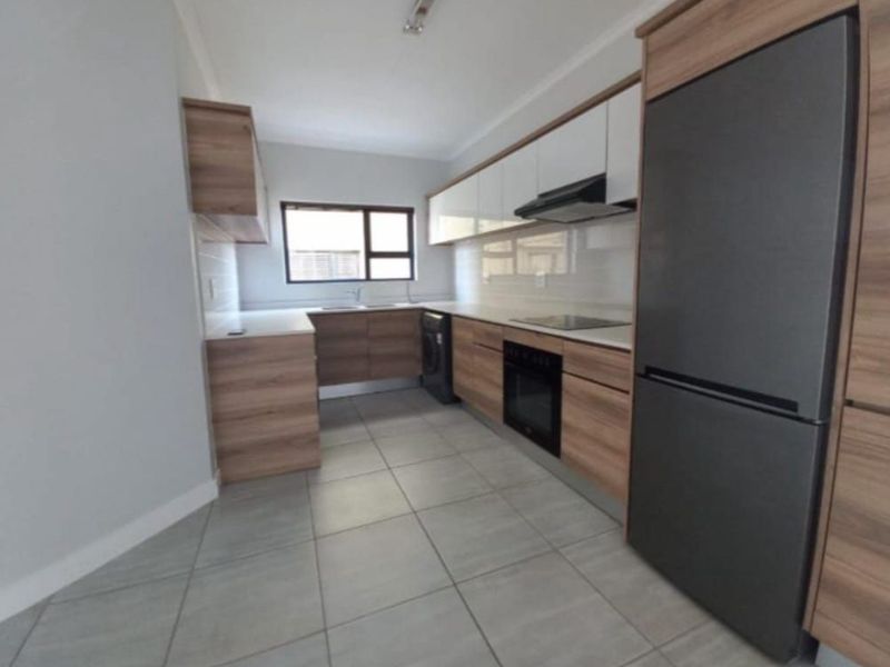 Modern kitchen featuring wood-grain cabinetry, white countertops, tiled backsplash, and integrated appliances including an oven and hob.