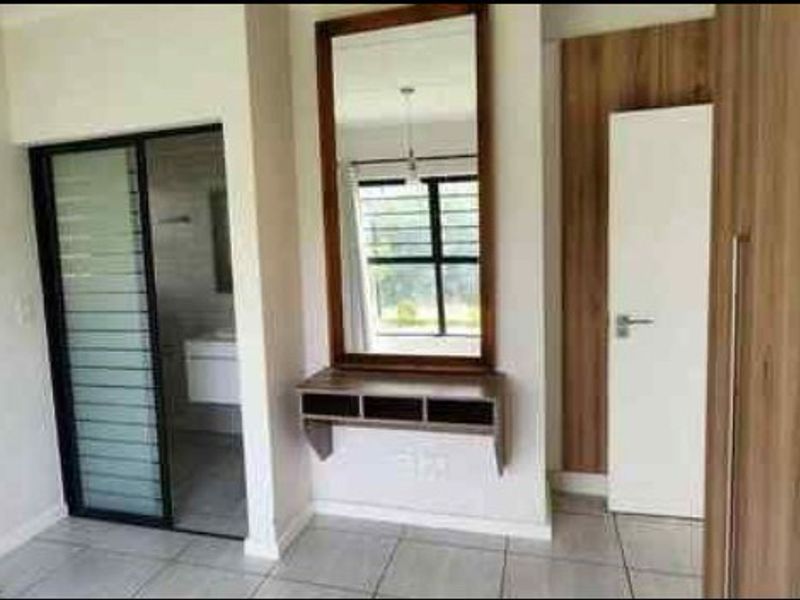 A bright bedroom featuring tiled flooring, built-in cupboards, a wall-mounted vanity with mirror, and direct access to an en-suite bathroom.