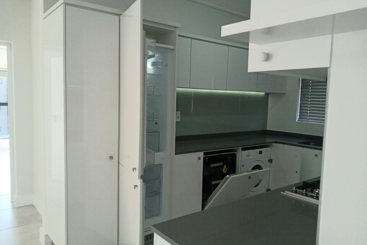 Modern kitchen featuring high-gloss cabinetry, integrated appliances, stone countertops, and a sleek glass splashback, offering a clean and contemporary aesthetic.