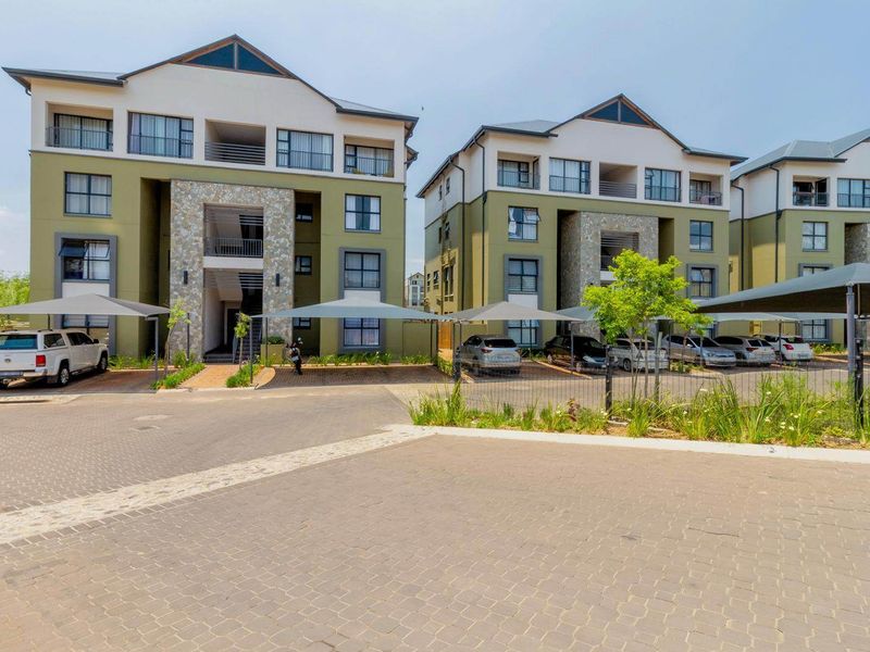 Front view of a modern apartment complex featuring stone-clad facades, paved parking areas, and dedicated shade cloth carports for residents.
