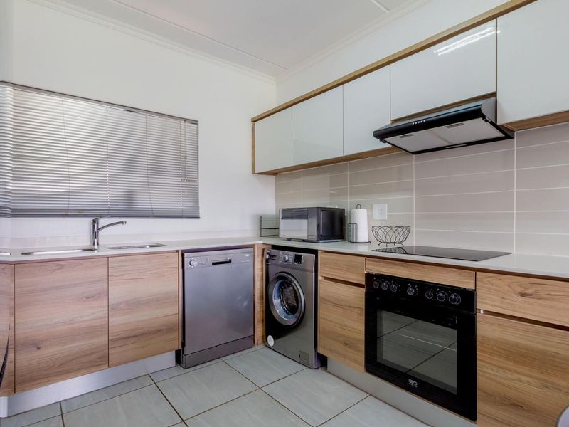 Modern kitchen featuring wood-finish cabinetry, stone countertops, integrated appliances, tiled backsplash, and a functional layout with ample storage.