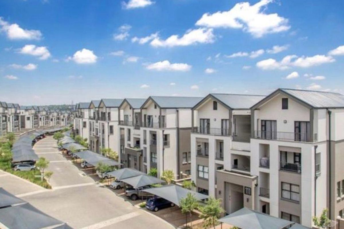 Aerial view of a modern apartment complex featuring multi-story residential buildings, paved driveways, and covered parking bays.