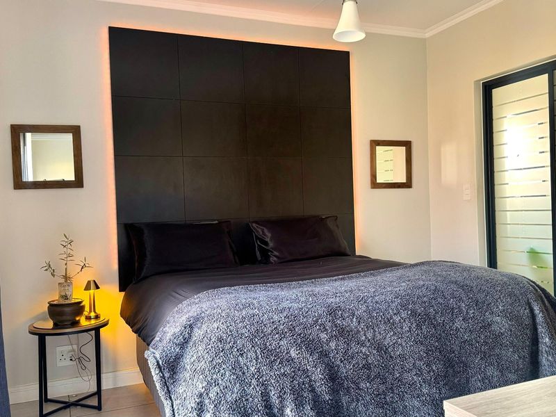 A modern bedroom featuring a dark, backlit feature wall panel, tiled flooring, and a sliding glass door providing natural light.