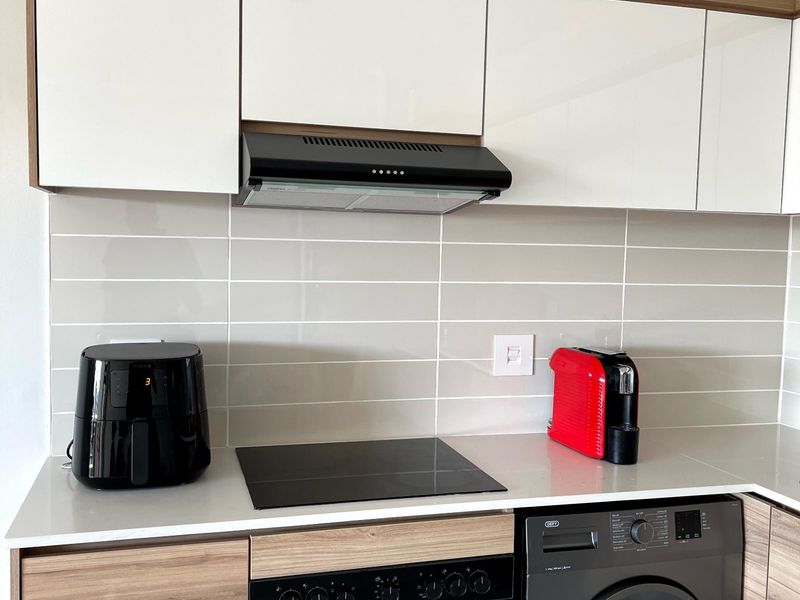 Modern kitchen featuring sleek white and wood-grain cabinetry, stone countertops, a built-in oven, ceramic hob, and a tiled backsplash.