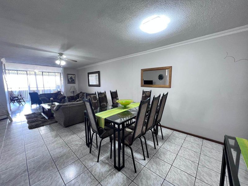 Spacious open-plan living and dining area featuring tiled flooring, a ceiling fan, and large sliding glass doors leading to an outdoor space.