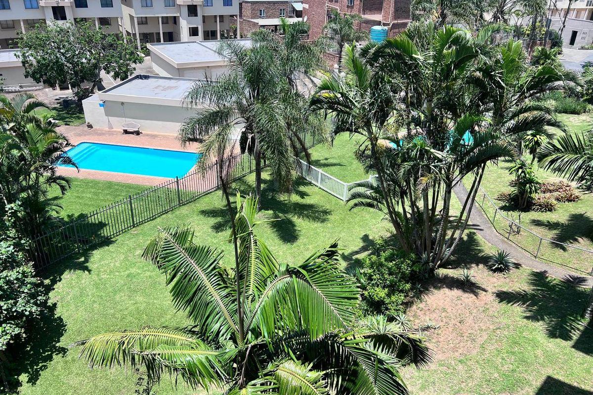 An elevated aerial view of a communal garden area featuring a swimming pool, lush palm trees, and well-maintained lawn spaces within an apartment complex.