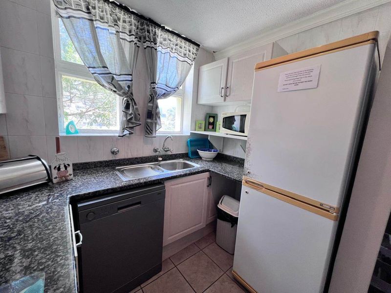 Compact kitchen featuring granite countertops, stainless steel sink, tiled backsplash, and built-in cabinetry, offering a functional workspace.